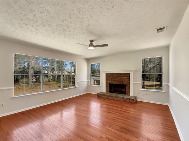 unfurnished living room with hardwood / wood-style flooring, a brick fireplace, and visible vents