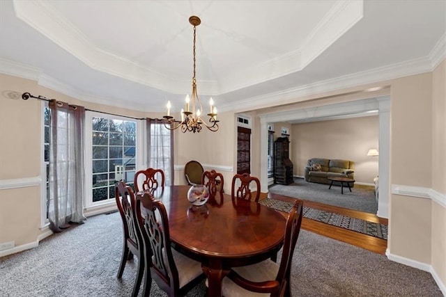 dining area featuring carpet floors, an inviting chandelier, a raised ceiling, and ornamental molding