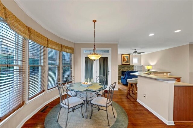 dining space featuring dark hardwood / wood-style flooring, a stone fireplace, ceiling fan, and crown molding