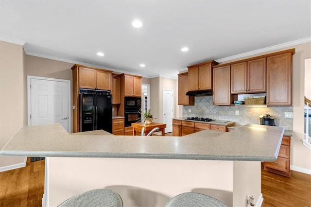 kitchen featuring tasteful backsplash, wood-type flooring, a kitchen bar, black appliances, and ornamental molding