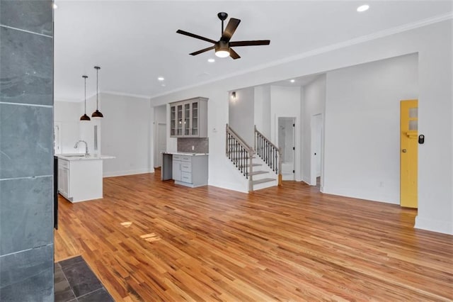 unfurnished living room with sink, ceiling fan, light hardwood / wood-style flooring, and ornamental molding