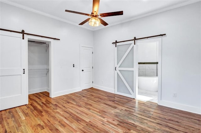 unfurnished bedroom featuring connected bathroom, ceiling fan, a barn door, and light wood-type flooring