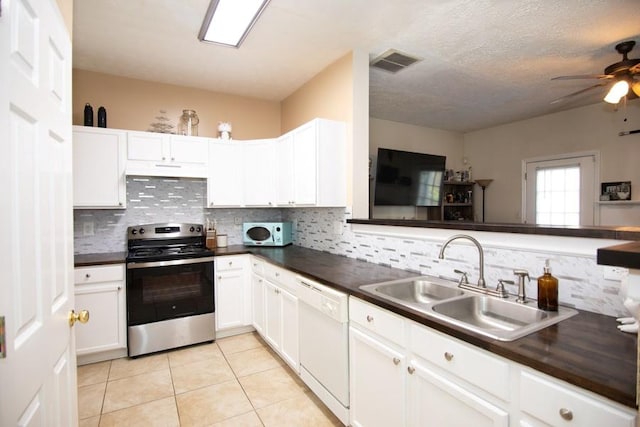 kitchen featuring visible vents, dark countertops, white appliances, tasteful backsplash, and a sink