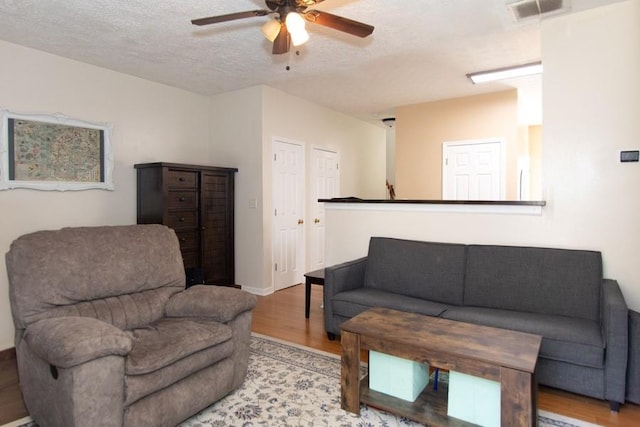 living room with visible vents, wood finished floors, baseboards, ceiling fan, and a textured ceiling