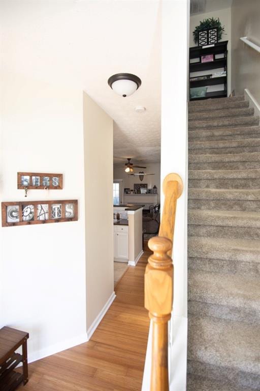 staircase with a ceiling fan, baseboards, and wood finished floors