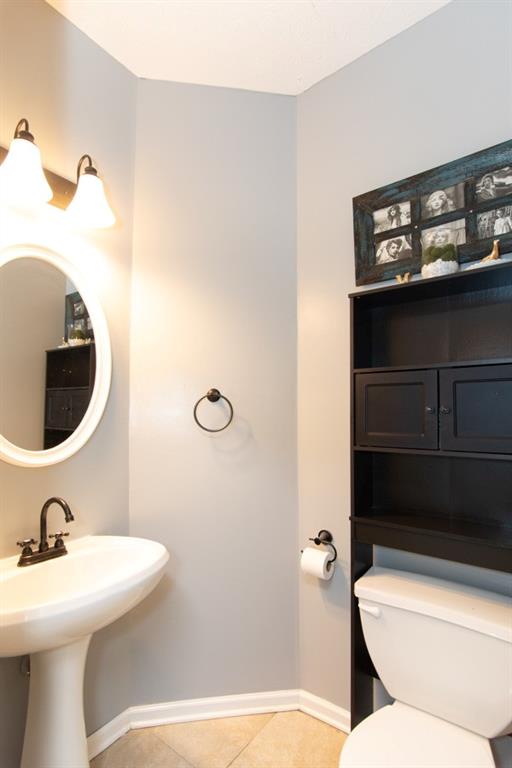 half bathroom with toilet, baseboards, a sink, and tile patterned flooring