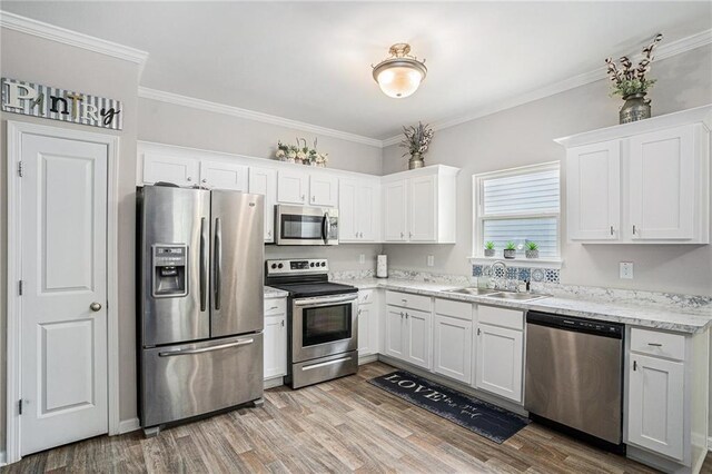 kitchen featuring appliances with stainless steel finishes, light stone counters, a sink, light wood finished floors, and white cabinetry