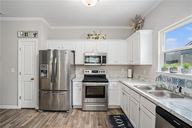 kitchen with ornamental molding, wood finished floors, white cabinets, a sink, and stainless steel appliances