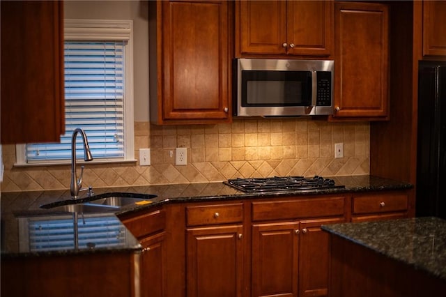 kitchen featuring stainless steel appliances, sink, dark stone countertops, and backsplash