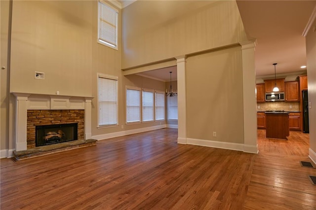 unfurnished living room with a stone fireplace, a towering ceiling, a chandelier, dark hardwood / wood-style flooring, and ornamental molding