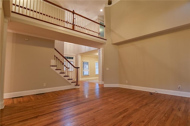 unfurnished living room featuring crown molding, hardwood / wood-style floors, and a high ceiling