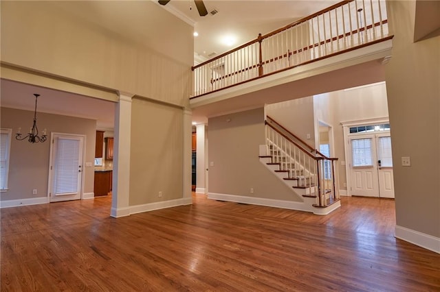 unfurnished living room featuring a high ceiling, dark hardwood / wood-style floors, and ceiling fan with notable chandelier