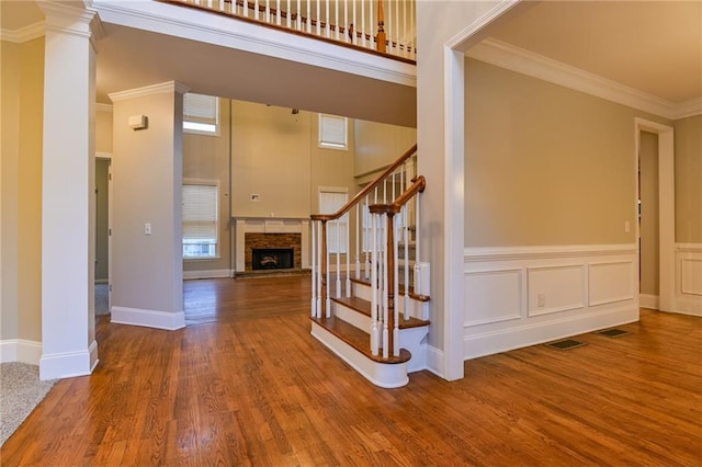 staircase featuring hardwood / wood-style floors, ornamental molding, decorative columns, and a fireplace