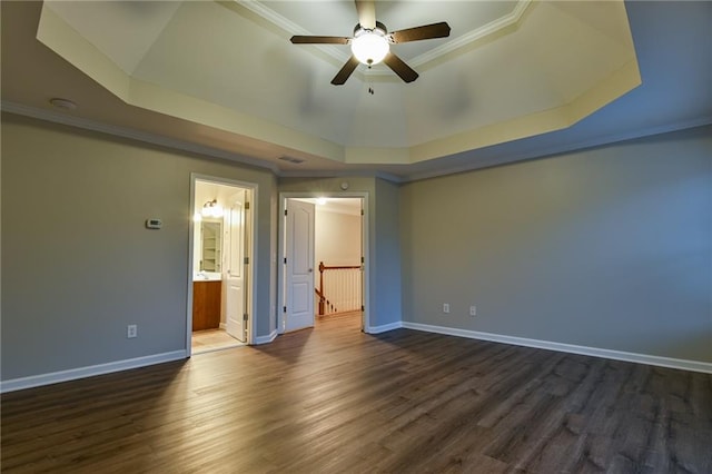 unfurnished bedroom with crown molding, connected bathroom, a tray ceiling, and dark hardwood / wood-style flooring