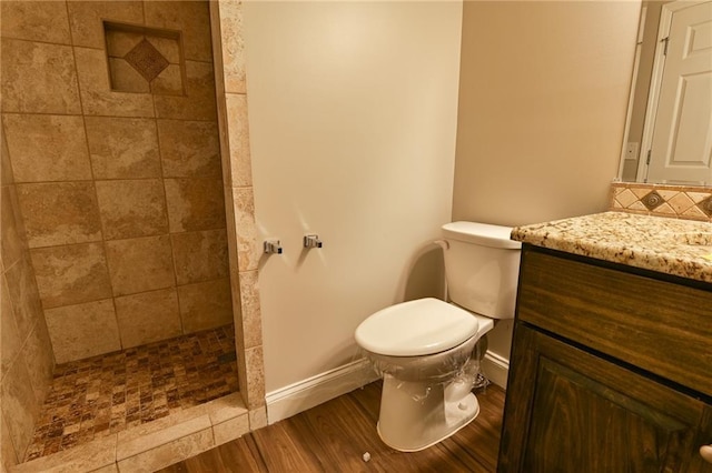 bathroom featuring hardwood / wood-style floors, vanity, a tile shower, decorative backsplash, and toilet