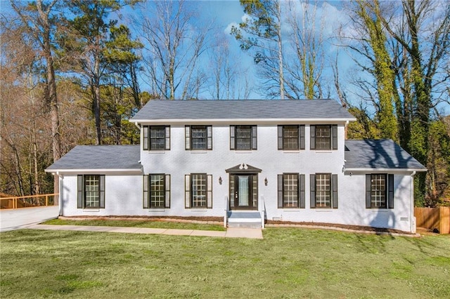 colonial-style house featuring brick siding, fence, and a front lawn