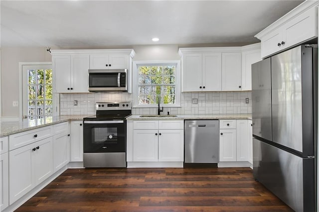 kitchen with dark wood finished floors, backsplash, appliances with stainless steel finishes, white cabinetry, and a sink