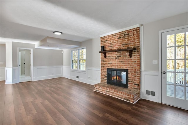 unfurnished living room featuring a wainscoted wall, dark wood-type flooring, a fireplace, and visible vents