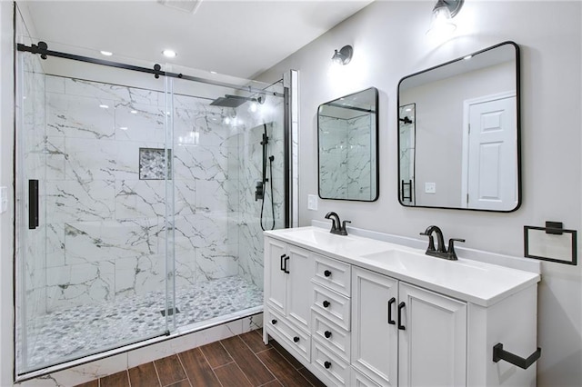 bathroom with wood finish floors, a sink, a marble finish shower, and double vanity