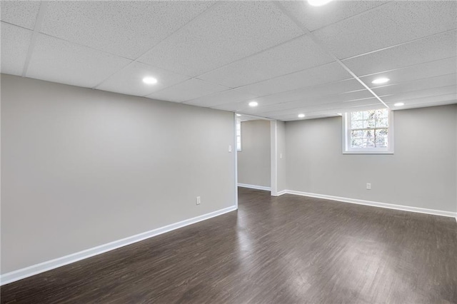 below grade area with dark wood-type flooring, recessed lighting, a drop ceiling, and baseboards