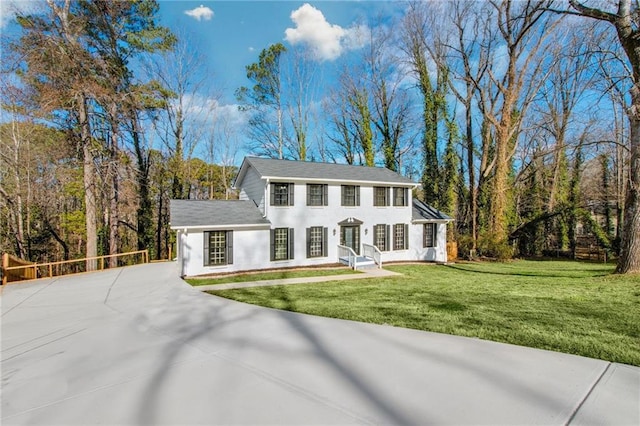 colonial home featuring concrete driveway, a front yard, and a wooded view