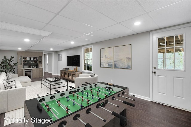 rec room with dark wood-style floors, beverage cooler, baseboards, and a drop ceiling