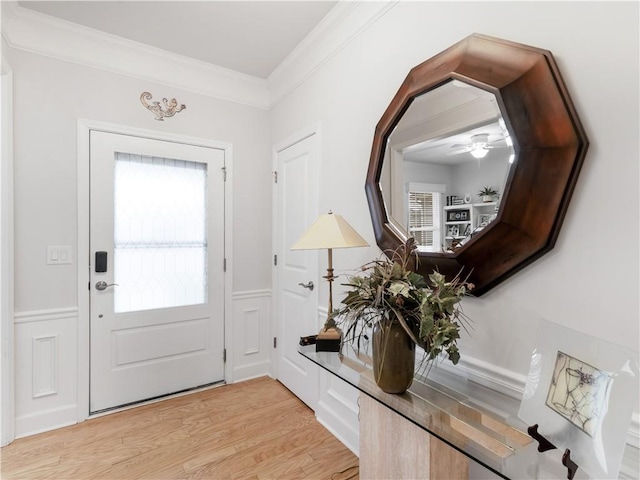 doorway featuring a wainscoted wall, crown molding, light wood-style flooring, and a decorative wall