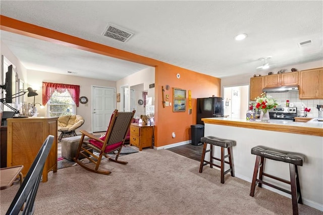 kitchen with under cabinet range hood, visible vents, freestanding refrigerator, decorative backsplash, and stainless steel range with electric stovetop