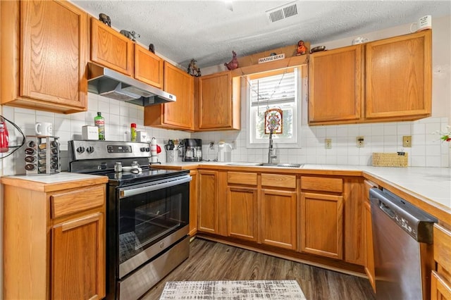 kitchen featuring dark wood-style floors, stainless steel appliances, visible vents, a sink, and under cabinet range hood