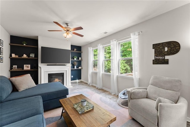 living room with ceiling fan, a glass covered fireplace, baseboards, and light wood-type flooring