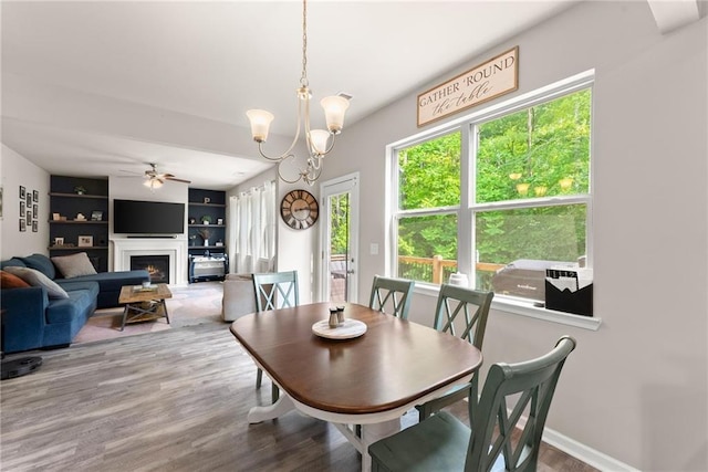 dining area featuring ceiling fan, wood finished floors, a lit fireplace, a chandelier, and baseboards