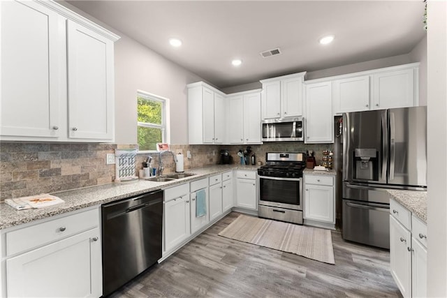 kitchen with appliances with stainless steel finishes, a sink, white cabinetry, tasteful backsplash, and light wood-type flooring