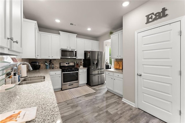 kitchen with appliances with stainless steel finishes, a sink, backsplash, white cabinets, and light wood-type flooring