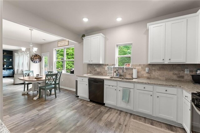 kitchen with a sink, black dishwasher, light wood-type flooring, white cabinets, and a chandelier