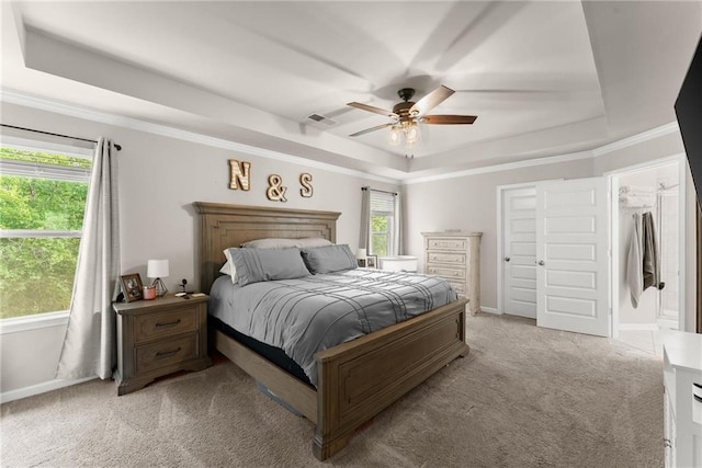 bedroom with a raised ceiling, light colored carpet, multiple windows, and ceiling fan