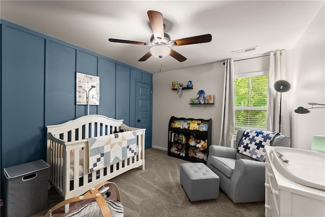 carpeted bedroom featuring a crib and a ceiling fan