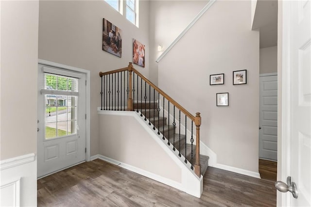 entryway featuring a towering ceiling, wood finished floors, baseboards, and stairs