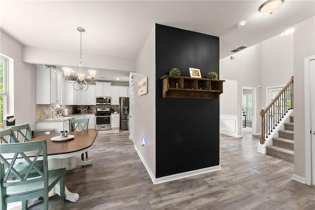 dining room featuring a chandelier, wood finished floors, stairs, baseboards, and high vaulted ceiling