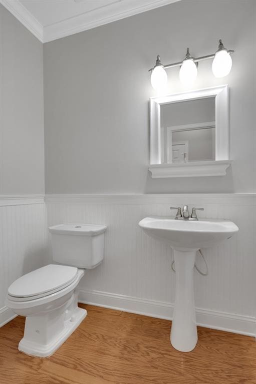 half bath with ornamental molding, wainscoting, toilet, and wood finished floors