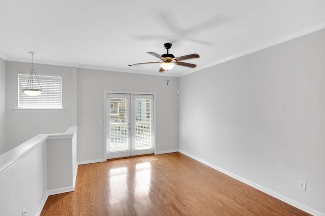 empty room featuring ceiling fan, crown molding, baseboards, and wood finished floors