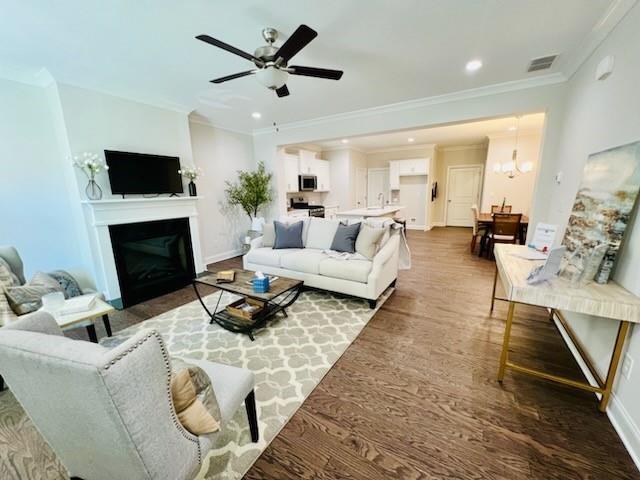 living room featuring crown molding, wood-type flooring, and ceiling fan with notable chandelier