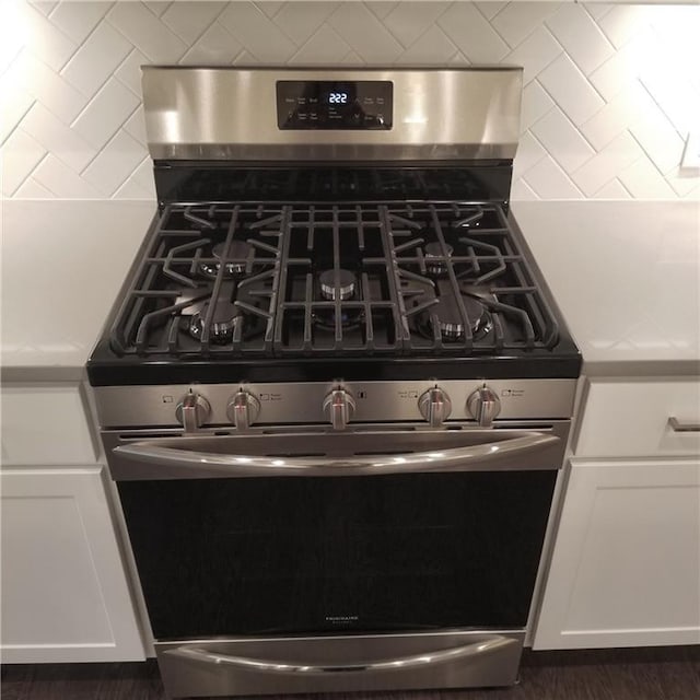 interior details with white cabinets, stainless steel range with gas stovetop, and backsplash