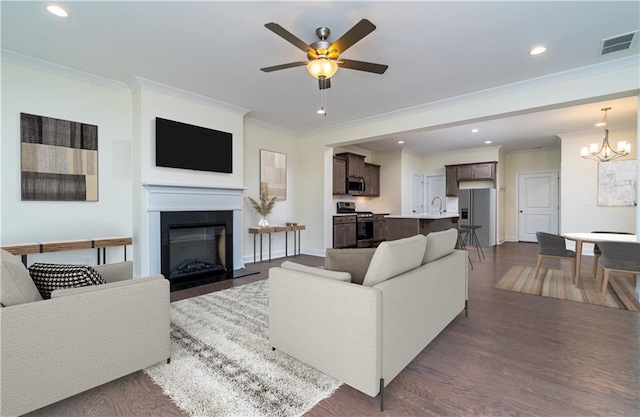 living room with crown molding, sink, dark wood-type flooring, and ceiling fan with notable chandelier