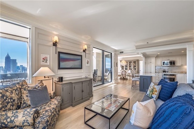 living area with a decorative wall, light wood-type flooring, visible vents, and crown molding