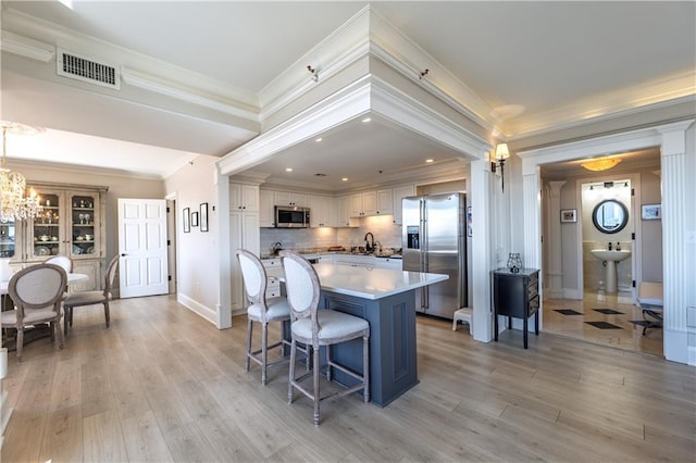 kitchen featuring crown molding, visible vents, light wood-style flooring, appliances with stainless steel finishes, and a kitchen breakfast bar