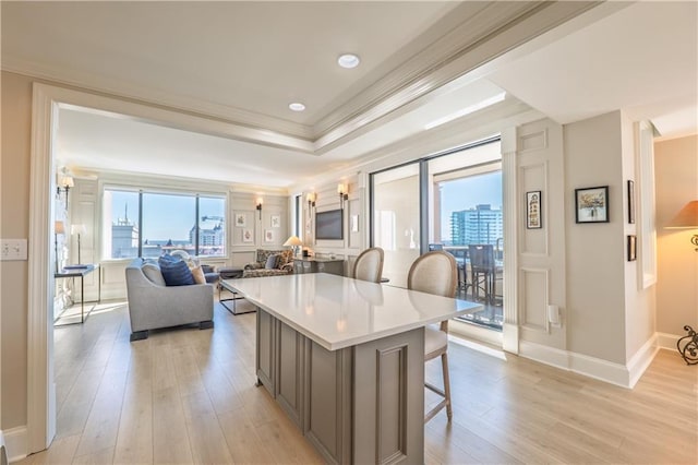 kitchen with a breakfast bar area, a raised ceiling, light countertops, ornamental molding, and light wood-type flooring