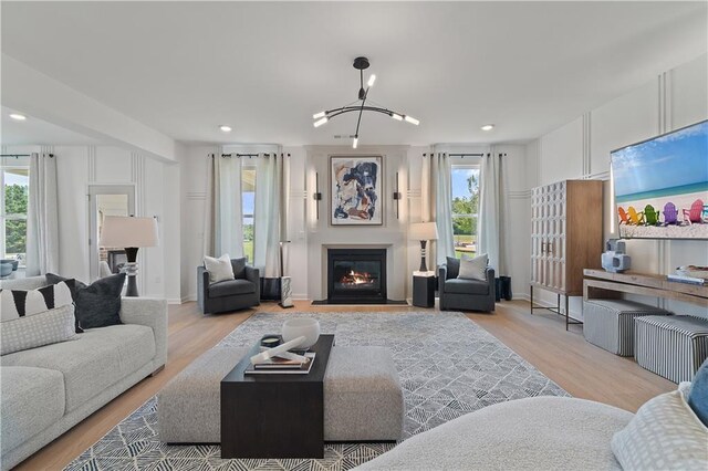 living room with light wood-type flooring, a healthy amount of sunlight, and an inviting chandelier