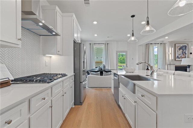 kitchen featuring appliances with stainless steel finishes, white cabinets, wall chimney exhaust hood, decorative light fixtures, and sink