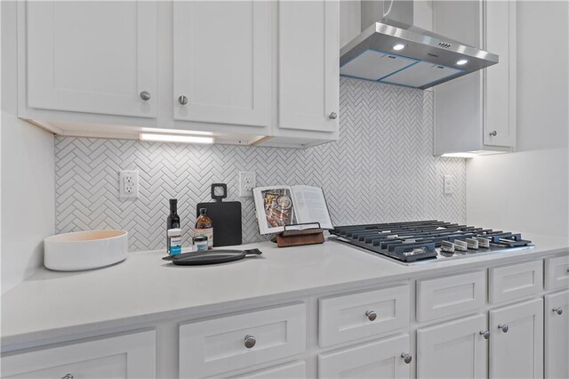 kitchen featuring backsplash, wall chimney exhaust hood, stainless steel gas cooktop, and white cabinets