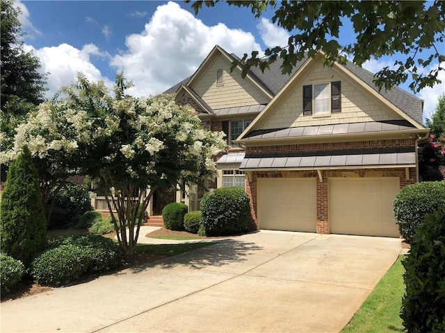 craftsman house with roof with shingles, a standing seam roof, an attached garage, concrete driveway, and brick siding